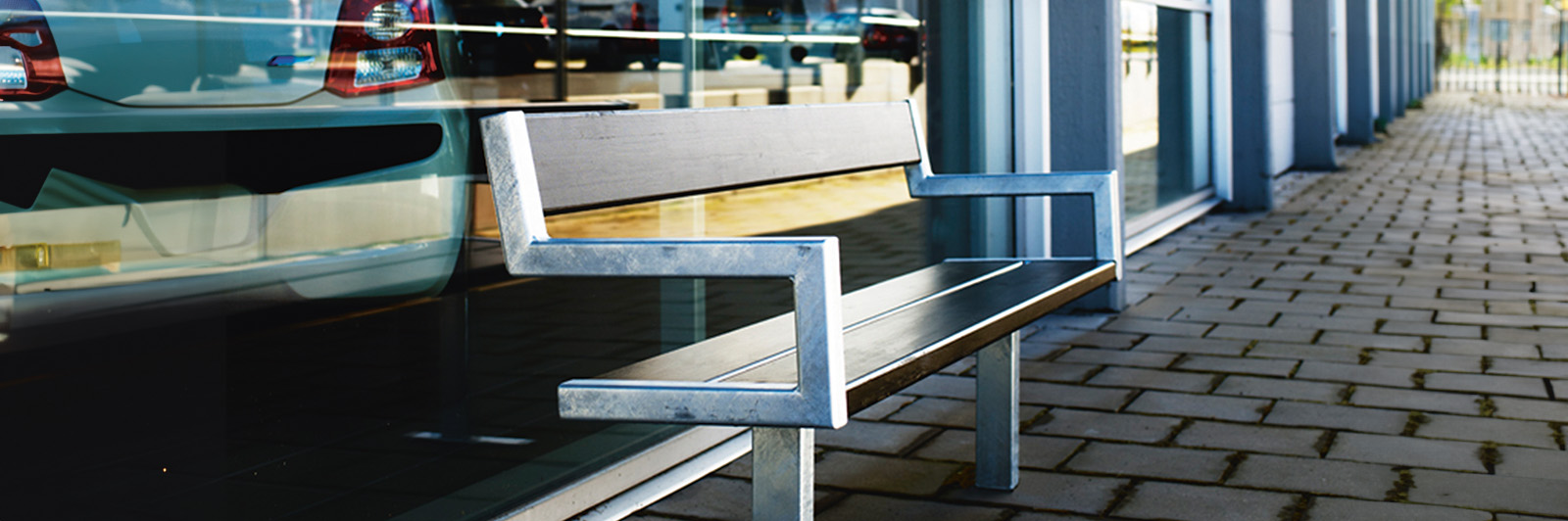 A steel architectural bench against a commercial building at sunset.